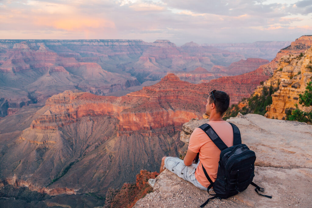 Young man sits at the edge of the Grand Canyon looking out